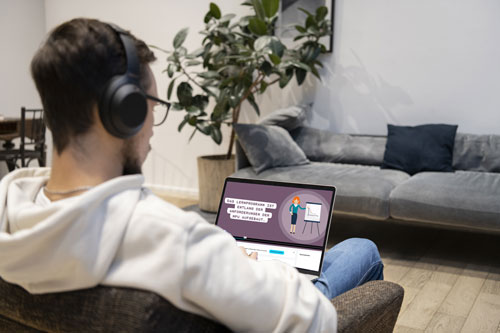 Mann sitzt auf der Couch vor dem Laptop und schaut ein Lernvideo.