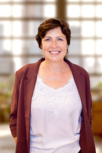 Portaitfoto frontal aufgenommen von Magdalena Pöhler mit großen Bürofenstern im Hintergrund.